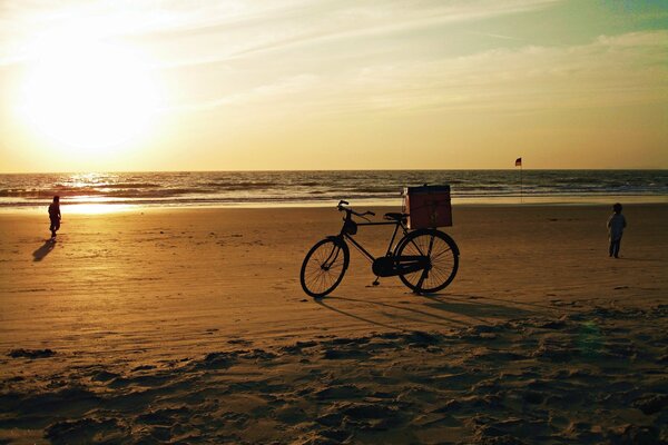 A bicycle standing on the sandy shore of the Indian Ocean against the background of the setting sun