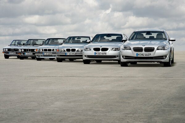 Six BMWs on the road against a cloudy sky