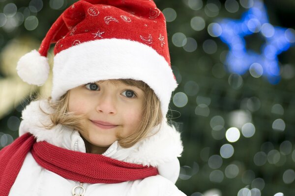 Fille avec un carré dans un chapeau de Noël. Fille aux yeux bleus dans le chapeau du père Noël. Photo de Noël avec des enfants. Fille sur fond d arbre de Noël