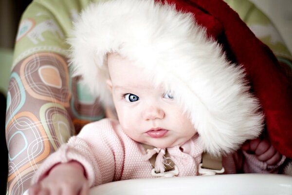 Bambino in un cappello di Capodanno. Bambino dagli occhi azzurri su un seggiolone