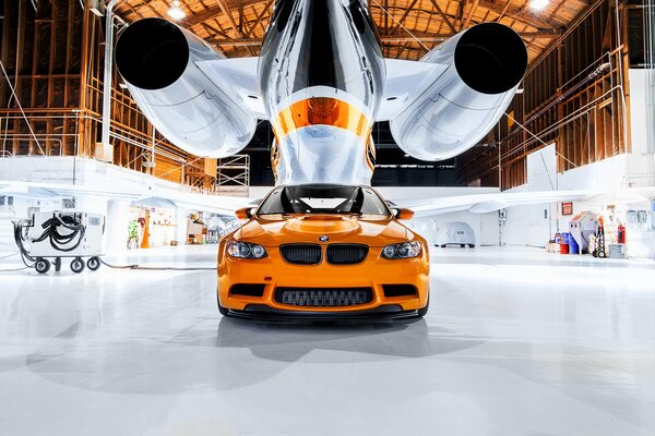 BMW naranja debajo del avión en el hangar