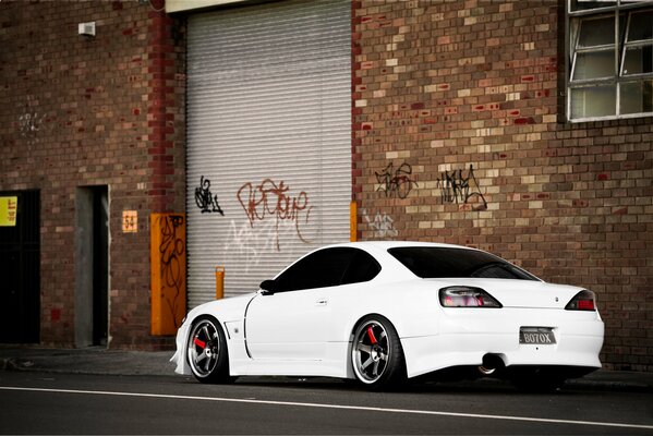 Weißer Nissan S15 Silvia steht vor dem Hintergrund eines Backsteingebäudes