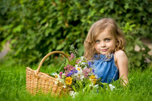 A girl with a basket of meadow flowers on a green lawn