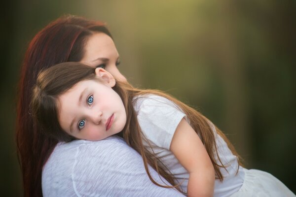 A blue-eyed girl lies with her head on her mother s shoulder