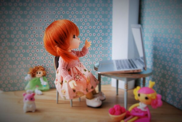 A doll in a pink dress. A composition of dolls. A doll behind a laptop. A doll with fiery hair and her friends