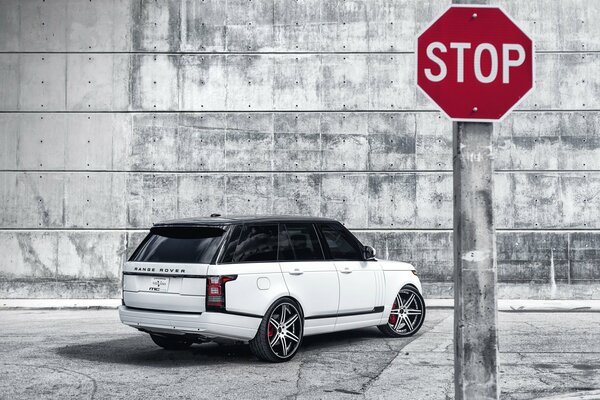 A stop sign on the van of a white range Rover and a stone wall
