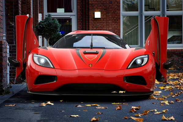 Voiture rouge sur fond de feuilles jaunes près de la maison