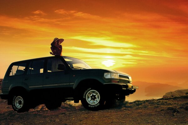 Ragazza sul tetto della jeep sullo sfondo del tramonto