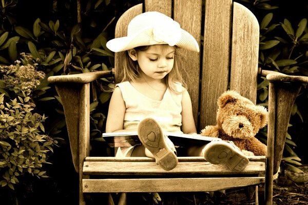 Photo in sepia. A girl in a hat with a bear. A girl is sitting on a high chair with a book and a friend a teddy bear