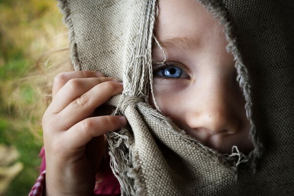 The girl looks through a slit in the burlap