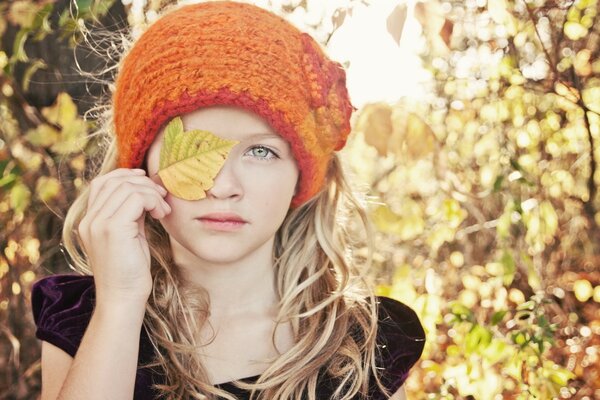 The girl covers one eye with a yellow leaf