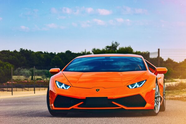 Orangefarbener Lamborghini Huracan fährt auf der Straße vor dem Hintergrund des Waldes