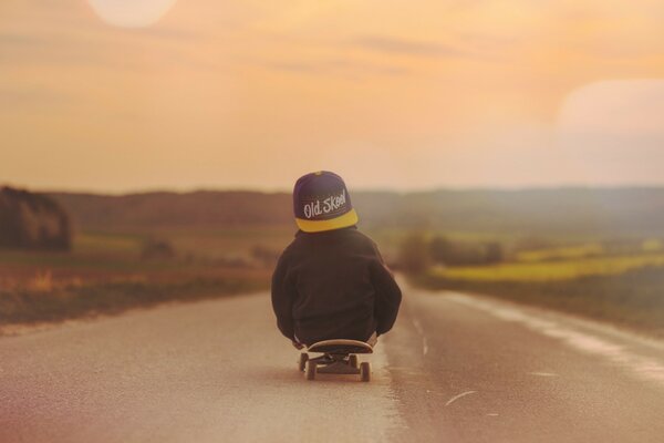 A boy on a skateboard looks at the sunset. Beautiful red sunset. A boy in a cap rides on the road