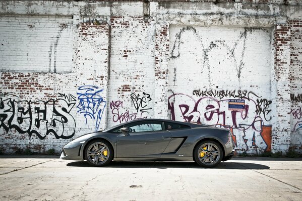 Coche Lamborghini gallardo gris contra fondo de pared con graffiti