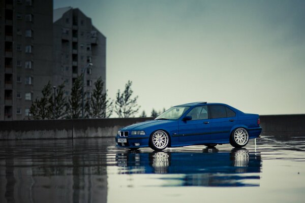 Coche azul BMW M3 E36 en asfalto mojado