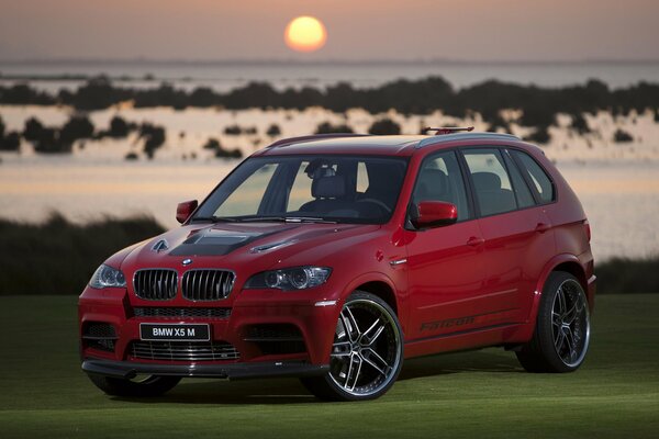 SUV bmw x5 sulla superficie verde al tramonto