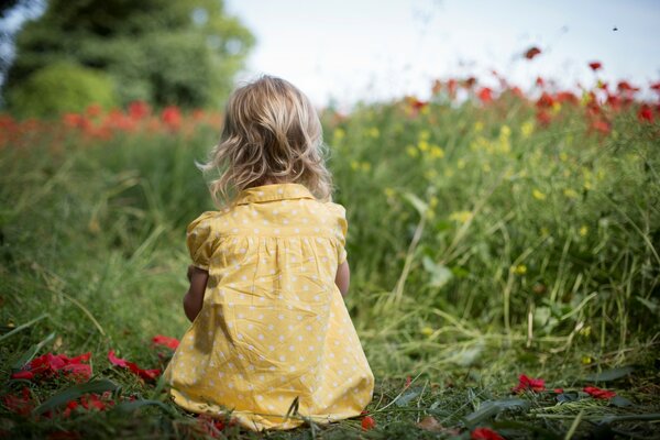 Petite fille en robe d été jaune est assis sur la Prairie