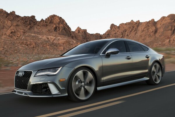 Gray Audi is driving on the road near the rocks