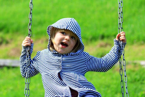 A child is swinging on a swing. A sweet girl smiles at summer