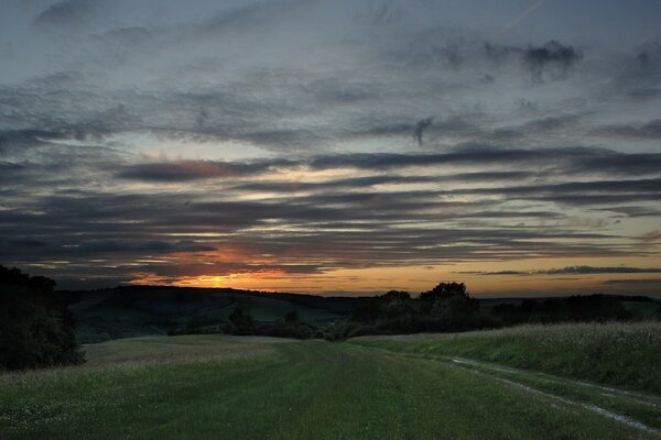 Die Straße führt zu den Hügeln. Sonnenuntergang mit Wolken