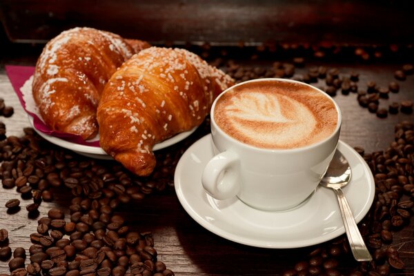 Croissants con una taza de café sobre un fondo de granos de café