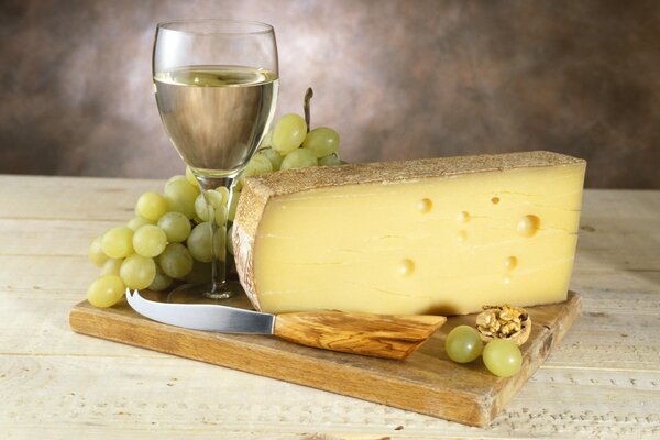 White wine in a glass with a bunch of grapes and delicious cheese