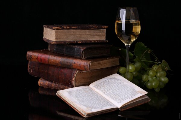 A stack of books, an open book, wine and green grapes on the table