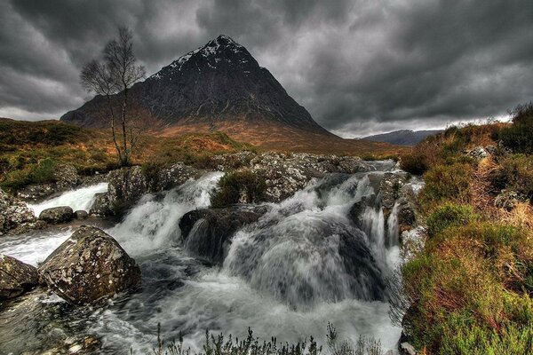 A fast river against the background of a mountain and a gray sky