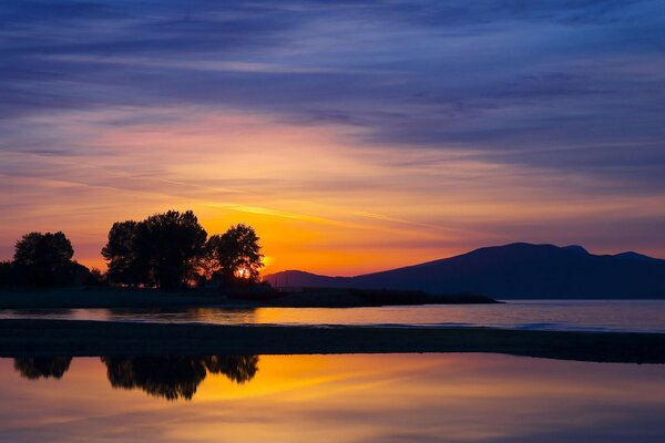 Puesta de sol naranja en la orilla al pie de las montañas