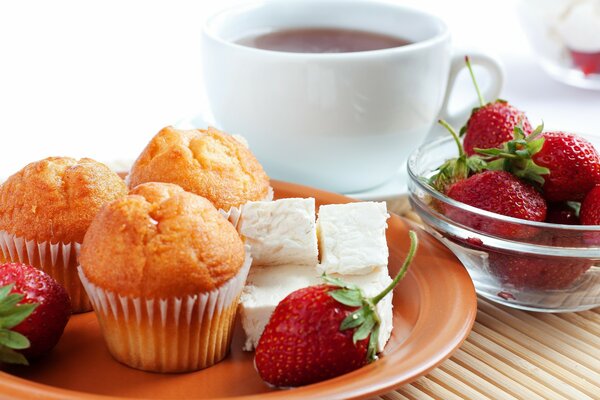 Magdalenas y fresas en un plato . En el fondo de una taza de té