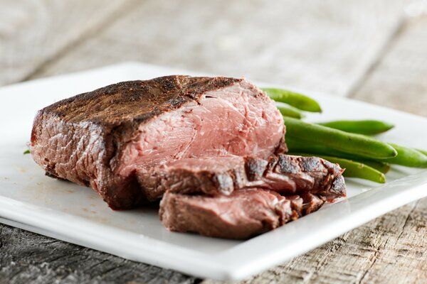 Steak with bean pods on a white plate