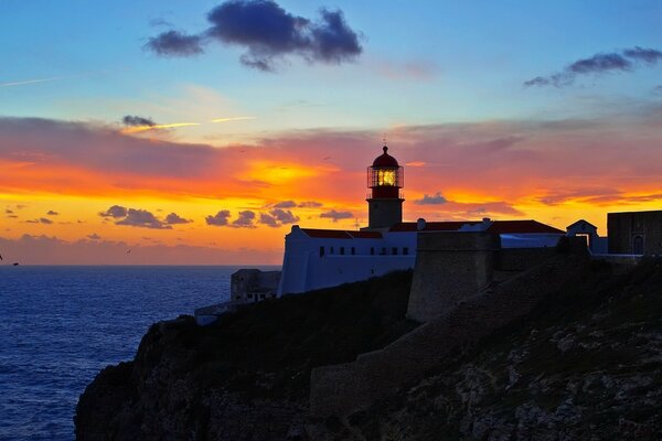 Lighthouse on the seashore against the background of sunset and clouds