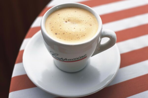 Cappuccino en una taza blanca sobre un mantel a rayas