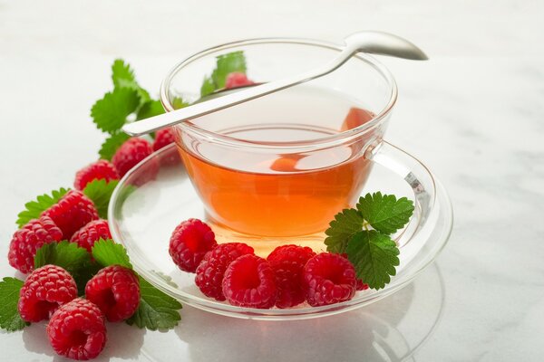 Tasse de thé et de framboises sur la soucoupe et la table