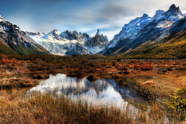 Mountains with blue snow are reflected in a puddle