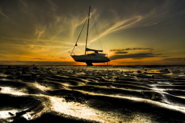 Un barco con una vela desinflada contra un cielo amarillo