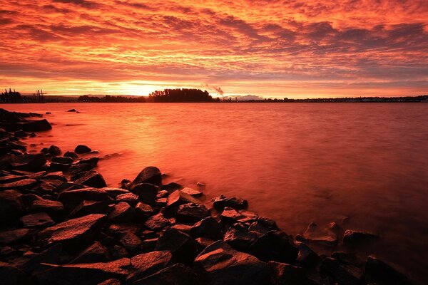 Puesta de sol roja. Costa rocosa del lago