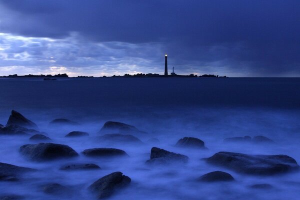 Rocks in the fog and a lighthouse in the distance