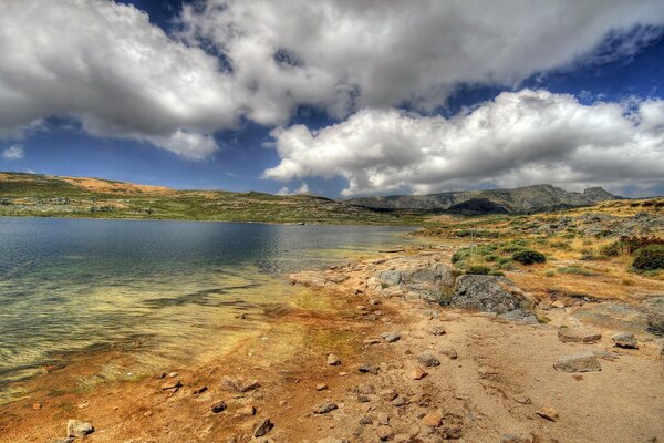 The rocky shore by the lake and the sky with clouds