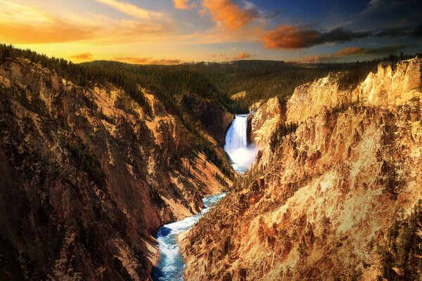 Schöner Sonnenuntergang Himmel. Ein Wasserfall in den Felsen von Yellowstone