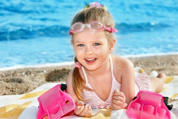 Ragazza dagli occhi azzurri sulla spiaggia con gli occhiali da nuoto sdraiata sulla spiaggia e sorridente