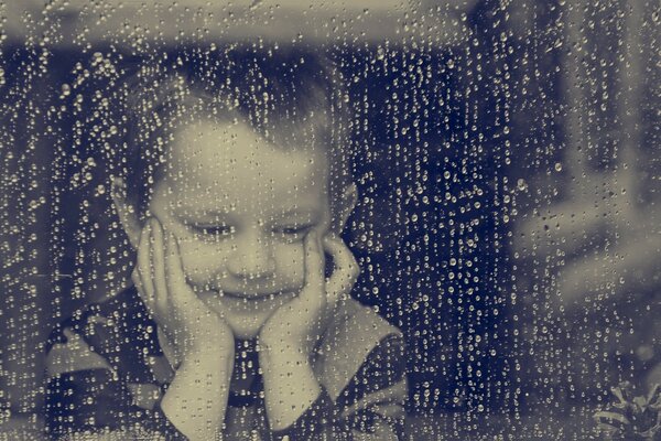 Junge schaut aus dem regnerischen Fenster