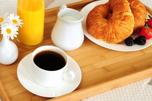 A cup of coffee with croissants, berries, milk and orange juice served for breakfast in bed