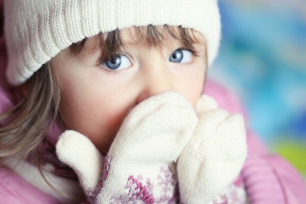 Fille aux yeux bleus couvre son visage avec ses mains dans des mitaines blanches chaudes