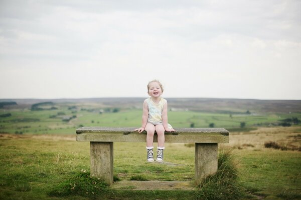 The child is sitting on a bench and smiling