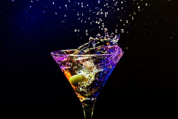 A magic-colored cocktail with an olive in a glass glass on a black background