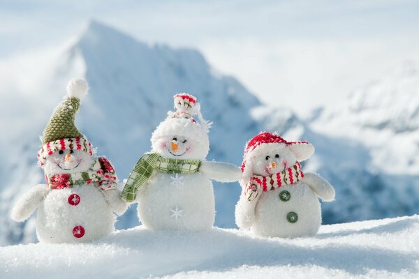 Tres pequeños muñecos de nieve con bufandas en el fondo de las montañas