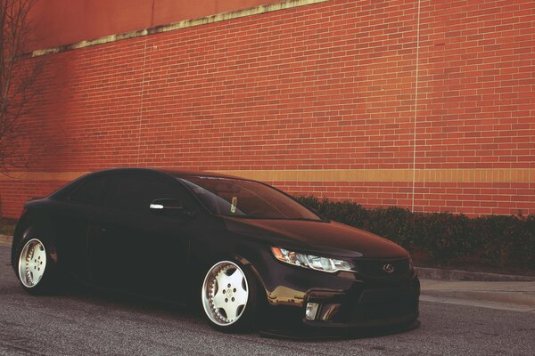 Tinted kia cerato with tuning on the background of a brick wall