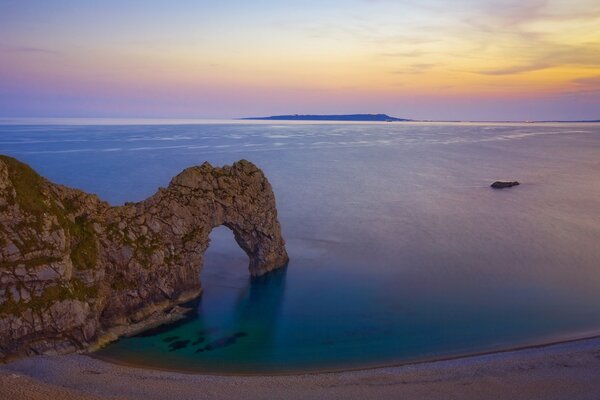 An arch made of a pile of stones standing in the water looks beautiful near the sky