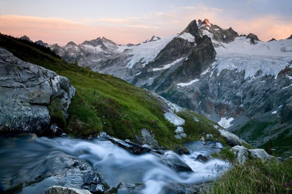 Arroyo en medio de montañas cubiertas de nieve y hierba